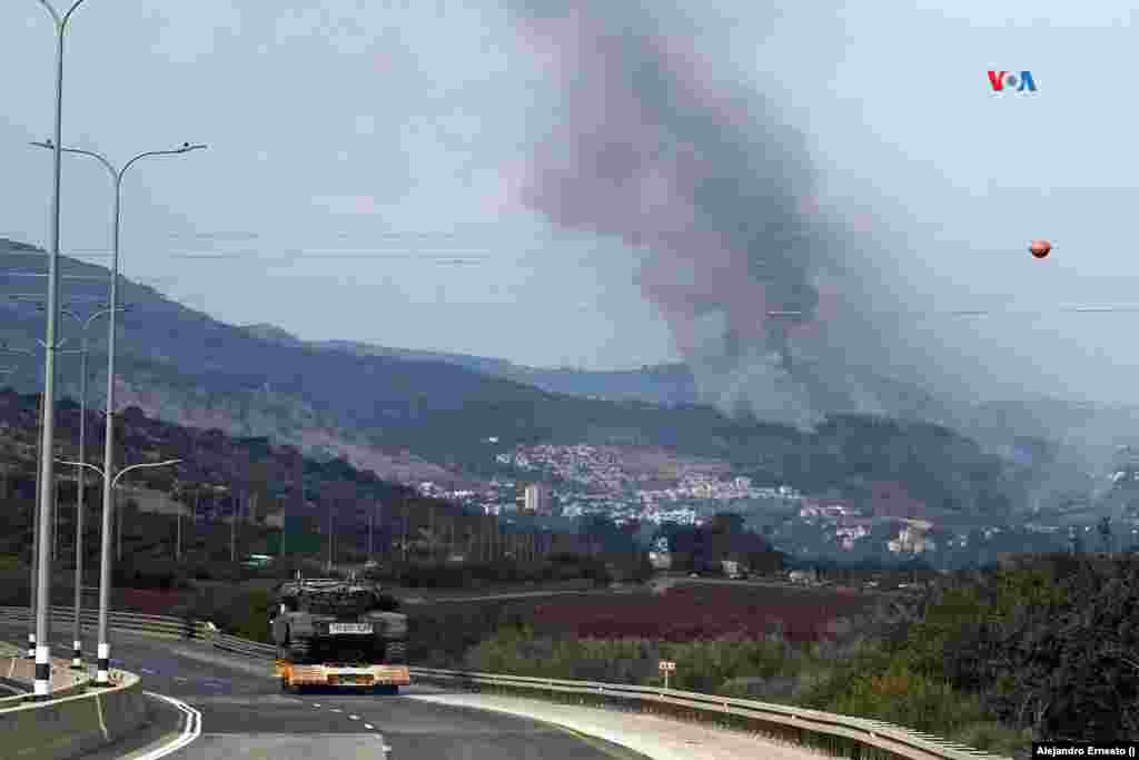 Un tanque israelí es transportado por una carretera, mientras se observa el humo del impacto de un proyectil lanzado desde el Líbano,&nbsp;el 31 de octubre de 2023.