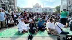Members of the Pan-Malaysian Islamic Party wait outside the Palace of Justice, background, as they await the Federal Court's decision on Kelantan state's sharia law criminal enactment, in Putrajaya, Malaysia, Feb. 9, 2024.