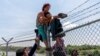 FILE - Migrants climb over a barbed wire fence after crossing the Rio Grande into US from Mexico, in Eagle Pass, Texas, Aug. 25, 2023. 