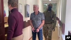 En esta fotografía tomada de un vídeo publicado por el Tribunal de Distrito de Lefortovo, Robert Shonov camina escoltado por agentes hasta la sala del Tribunal de Distrito de Lefortovo en Moscú, el 18 de mayo de 2023.