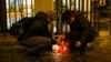 A woman lights candles near the philosophy building at Charles University in Prague, Czech Republic, Dec. 21, 2023. A Czech student on Thursday shot and killed his father, then shot and killed at least 14 people at the university, police said. His body was found at the scene. 
