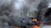 Motociclistas pasan a través de columnas de humo en medio de protestas por una escasez de combustible que se ha intensificado por la violencia entre pandillas en Puerto Príncipe, Haití, el 13 de julio de 2022. Foto AP.