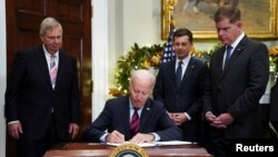 El presidente Biden, flanqueado por el secretario de Agricultura, Tom Vilsack (izq.), el secretario de Transporte, Pete Buttigieg, y el secretario de Trabajo, Matt Walsh, firma la legislación ferroviaria para evitar una huelga en todo el país, el 2 de diciembre de 2022.