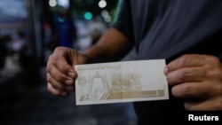 ARCHIVO - Un hombre muestra un billete venezolano de 5 bolívares en octubre de 2021.