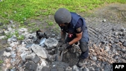 Experto en explosivos extrae fragmento de misil ruso en el territorio del Monumento a las Víctimas del Totalitarismo en las afueras del norte de la ciudad ucraniana de Járkov, el 8 de mayo de 2022. (Foto de SERGEY BOBOK / AFP)