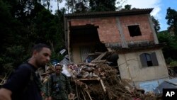 ARCHIVO - Oficiales militares pasan frente a una casa dañada por un deslizamiento de tierra, en Petrópolis, estado de Río de Janeiro, Brasil, el martes 22 de febrero de 2022.