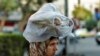 FILE - A woman carries bread on her head in Damascus, Syria, July 24, 2019. In October 2020, the government limited the amount of subsidized bread families could buy. And the market price of bread increased 26% from September to October.