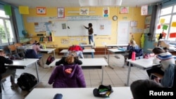 A teacher, wearing a protective face mask, teaches to schoolchildren in a classroom at a private school during its reopening in Saint-Sebastien-sur-Loire near Nantes.