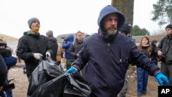 Policët mbartin kufomën e një civili të gjendur në Bucha (5 prill 2022)