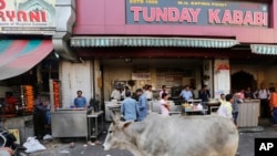 FILE - A cow walks in front of Tundey Kababi, a 105-year-old kabab institution in Lucknow, India, March 31, 2017. 