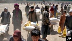 Un combatiente del Talibán vigila mientras varias personas reciben raciones de comida distribuidas por un grupo de ayuda humanitaria de China, en Kabul, Afganistán, el sábado 30 de abril de 2022. 