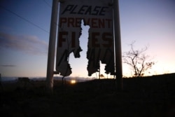 A car drives by a burnt roadside sign that says, "Please Prevent Fires, Mahalo," Aug. 5, 2021, in Waimea, Hawaii.
