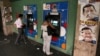 FILE - People withdraw money from cash machines where election propaganda supporting Venezuela&#39;s President Hugo Chavez cover the nearby walls in Caracas, Venezuela, Feb. 8, 2013.