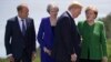 European Council President Donald Tusk,from left, British Prime Minister Theresa May and German Chancellor Angela Merkel look on as U.S. President Donald Trump arrives for the group photo at the G-7 Summit, June 8, 2018. 