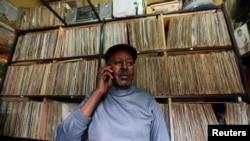 FILE - Vendor James Rugami talks to a customer on his cell phone inside his shop that specialize in selling second-hand vinyl records and vintage players at the Kenyatta Market in Nairobi, Nov. 24, 2016. 
