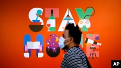 A man wearing a face mask walks in front of a poster recommending people to stay at home, at a department store in Berlin, Germany, April 20, 2020. 