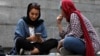 FILE - A woman checks her cell phone sitting with a companion on the steps outside a shopping mall in northern Tehran, Iran, July 2, 2019.