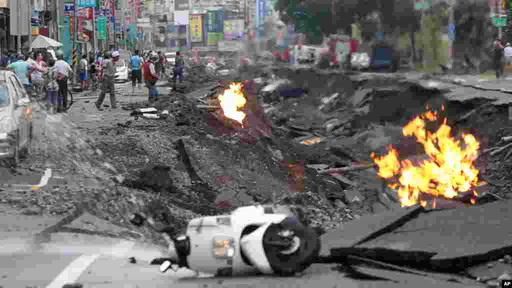 Vehicles are left lying on a destroyed street as part of the street is burning with flame following multiple explosions from an underground gas leak in Kaohsiung, Taiwan, Aug. 1, 2014. 