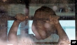 Un niño inmigrante mira desde un autobús de la Patrulla Fronteriza de EE.UU. mientras manifestantes bloqueaban la calle frente al Centro de Procesamiento Central de la Patrulla Fronteriza de los Estados Unidos el sábado 23 de junio de 2018 en McAllen, Texas.