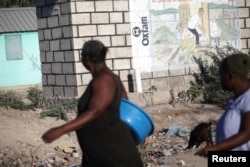 FILE - People walk past an Oxfam sign in Corail, a camp for people displaced by the 2010 earthquake, on the outskirts of Port-au-Prince, Haiti, Feb. 16, 2018.