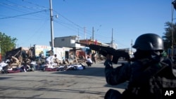 Un agente de la policía nacional de Haití dispara a manifestantes mientras sus colegas se cubren después de que se escucharan disparos al final de una ceremonia por el 212 aniversario del asesinato del héroe de la independencia Jean-Jacques Dessalines, en Puerto Príncipe. Oct. 17 de 2018.