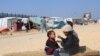 Seorang anak perempuan Palestina tampak menyuapi adiknya makanan di dekat tenda pengungsi di Rafah, tempat mereka kini tinggal, pada 25 Februari 2024. (Foto: Reuters/Saleh Salem)