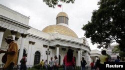 ARCHIVO - La gente pasa frente al edificio de la Asamblea Nacional en Caracas, Venezuela, durante una sesión parlamentaria, el 14 de diciembre de 2016.