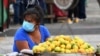 Archivo - Una mujer usa una máscara facial mientras espera clientes en un mercado en Tegucigalpa.