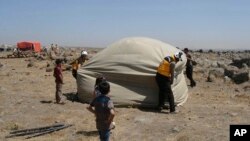This photo, released by the Syrian Civil Defense White Helmets, shows civil defense workers setting up a tent for civilians who fled from Daraa after shelling by Syrian government forces, in the town of Qunaitra, southwestern Syria, June 28, 2018.