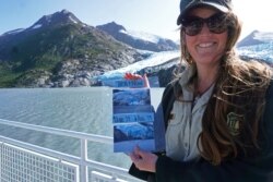 FILE - Chugach National Forest ranger Megan Parsley holds photos showing this summer's ice loss at the face of Portage Glacier, Alaska, Aug. 17, 2019.