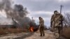 Tentara Ukraina melewati bus sukarelawan yang terbakar setelah drone Rusia menabraknya di dekat Bakhmut, wilayah Donetsk, Ukraina, Kamis, 23 November 2023. (Foto: via AP)