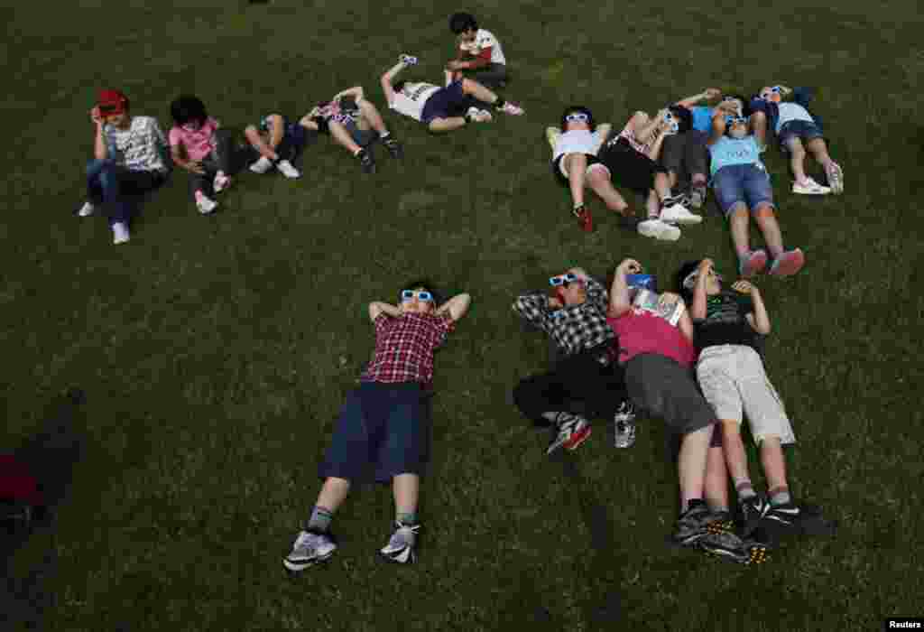 School children using solar viewers lie down on a lawn as they observe an annular eclipse at Hirai Daini Elementary School, Tokyo, Japan, May 21, 2012. Un grupo de estudiantes Hirai Daini, escuela primaria de Tokio, Japón, utilizan protectores para
