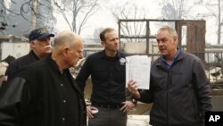 El gobernador de California, Jerry Brown, segundo a la izquierda, mira el libro de trabajo de los estudiantes presentado por el secretario del Interior Ryan Zinke, que se encontró durante un recorrido por la Escuela Primaria Paradise, devastada por el fuego.