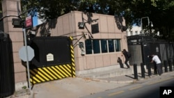 Periodistas toman fotos del daño a una puerta del puesto de seguridad por disparos efectuados desde un automóvil en movimiento frente a la embajada de EE.UU. en Ankara, Turquía, el lunes, 20 de agosto de 2018.