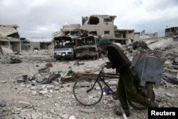 FILE - A man walks with his bicycle through a debris-littered site in the besieged town of Douma, eastern Ghouta, near Damascus, Syria, March 30, 2018.
