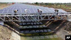 FILE - Indian workers add finishing touches to installed solar panels covering the Narmada canal at Chandrasan village, about 40 kilometers from Ahmadabad, India, April 22, 2012. 