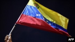 Un hombre muestra una bandera venezolana mientras familiares y amigos de migrantes venezolanos que murieron cuando se hundió la embarcación que los transportaba a Trinidad y Tobago, protestan en Guiria, Venezuela, el 18 de diciembre de 2020.