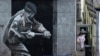 FILE - A woman takes out her rubbish beside a mural depicting a British soldier knocking down the door of a house with a sledge hammer in Derry, Northern Ireland, March 23, 2010. The Bloody Sunday massacre took place in Derry in 1972.