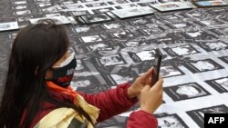 Una mujer toma una fotografía de pancartas con las imágenes de víctima del conflicto colombiano colocadas en el pavimento durante una manifestación frente a la sede de la Unión Europea en Bogotá, el 9 de abril de 2021.