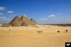 FILE - In this April 9, 2015 image tourists ride camels at the historical site of the Giza Pyramids in Giza, near Cairo, Egypt.