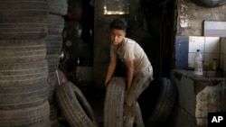 Un niño lleva una llanta hacia un taller de reparación donde trabaja en El Cairo, Egipto, el miércoles, 12 de junio de 2019.