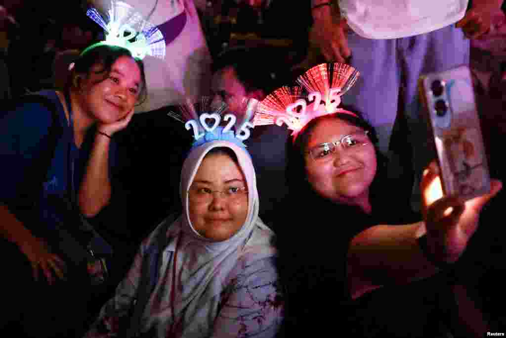 Para wanita yang mengenakan ikat kepala bertuliskan &#39;2025&#39; mengambil foto swafoto selama perayaan Malam Tahun Baru di Jakarta, 31 Desember 2024. (Reuters)&nbsp;