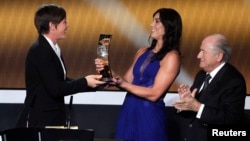 FILE - Sepp Blatter, then the head of FIFA, applauds as Hope Solo, second from right, presents a trophy to fellow soccer player Abby Wambach during the FIFA Ballon d'Or 2012 awards ceremony in Zurich, Jan. 7, 2013. Solo now says Blatter groped her just before she got on stage. 