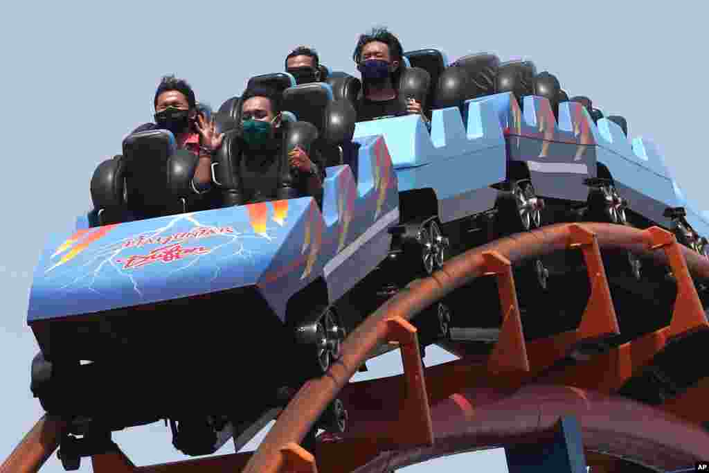 Hombres indonesios que llevan máscaras protectoras y se sientan separados mientras disfrutan de un paseo en el parque de atracciones Dunia Fantasi en el primer día de reapertura luego de semanas de cierre debido a las restricciones del coronavirus.