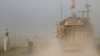 FILE - A man gestures at U.S military vehicles driving in the town of Darbasiya, Syria, next to the Turkish border, April 28, 2017. 