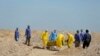FILE - Iraqi health ministry workers carry a coffin of a person who died from coronavirus infection at a new cemetery for people who died from COVID-19, outside the town of Najaf, Iraq, March 30, 2020.