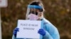 Medical assistant Miriam Fuentes gives a patient instructions via sign at a drive-through COVID-19 coronavirus testing station for University of Washington Medicine patients Tuesday, March 17, 2020, in Seattle. 