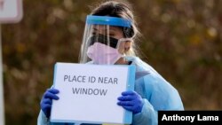 Medical assistant Miriam Fuentes gives a patient instructions via sign at a drive-through COVID-19 coronavirus testing station for University of Washington Medicine patients Tuesday, March 17, 2020, in Seattle. 