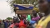 FILE - A woman balances a reed basket holding her child on her head as she stands with fellow villagers waiting to receive food rations at a village in Ayod county, South Sudan, Feb. 6, 2020.