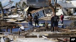 Gente de pie en el puente destruido a Pine Island mientras contemplan los daños causados por el huracán Ian en Matlacha, Florida, el domingo 2 de octubre de 2022. El único puente a la isla estaba muy dañado y sólo se podía acceder por mar o aire. (AP Foto/Gerald Herbert)
